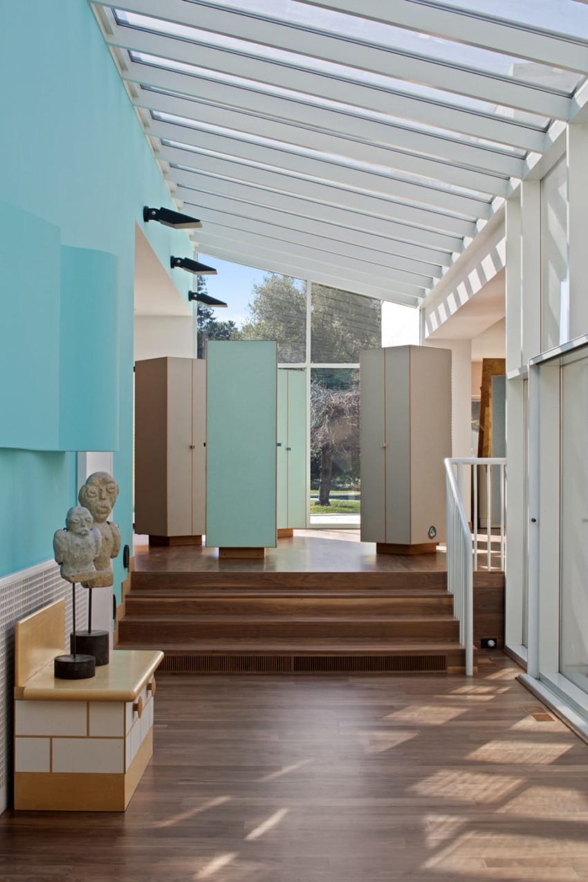 Modern room with large windows, blue walls, wooden floors, and unique sculpture on table in bright natural light.