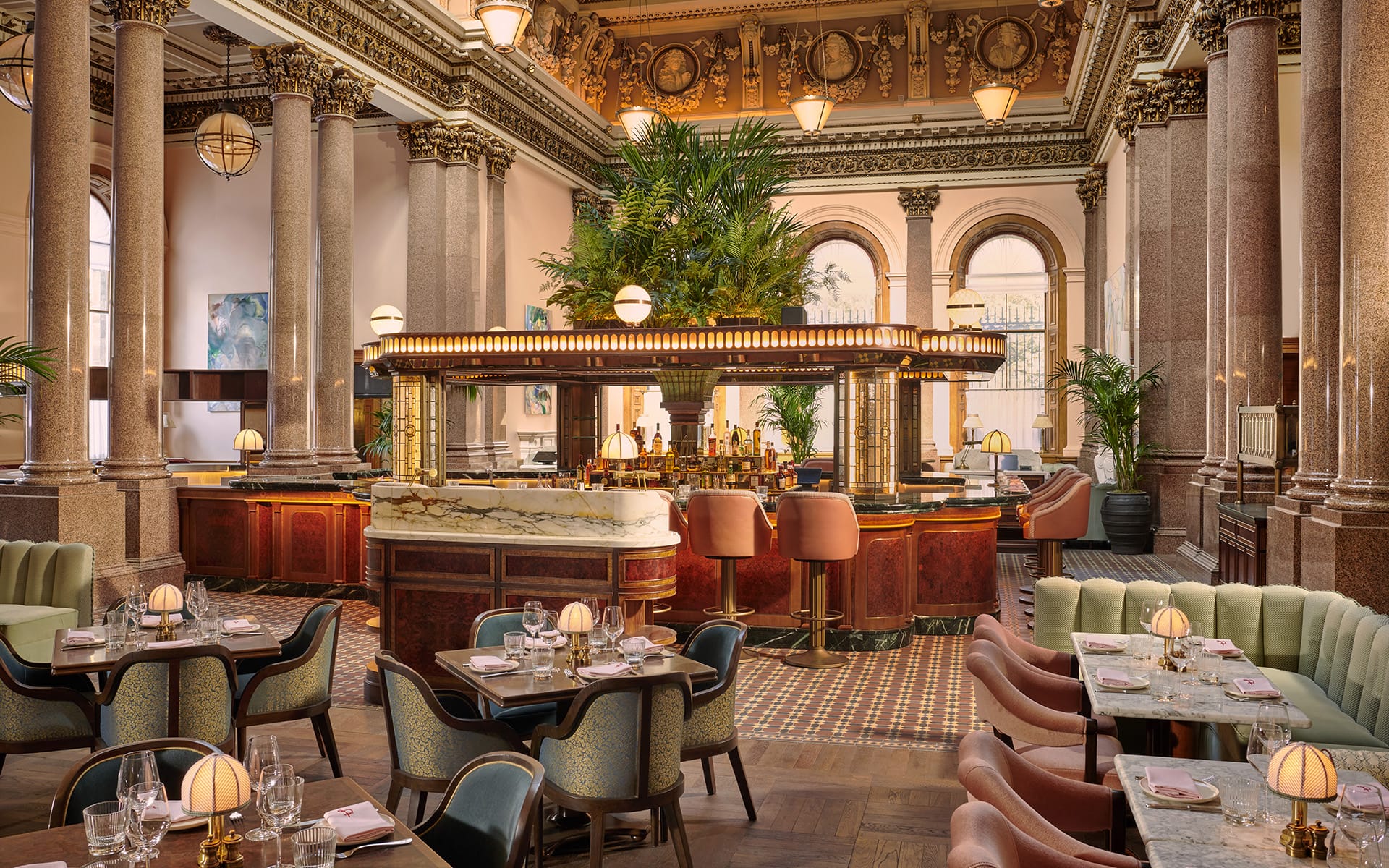 Upscale restaurant interior with ornate columns, elegant seating, and a central bar surrounded by plush armchairs.