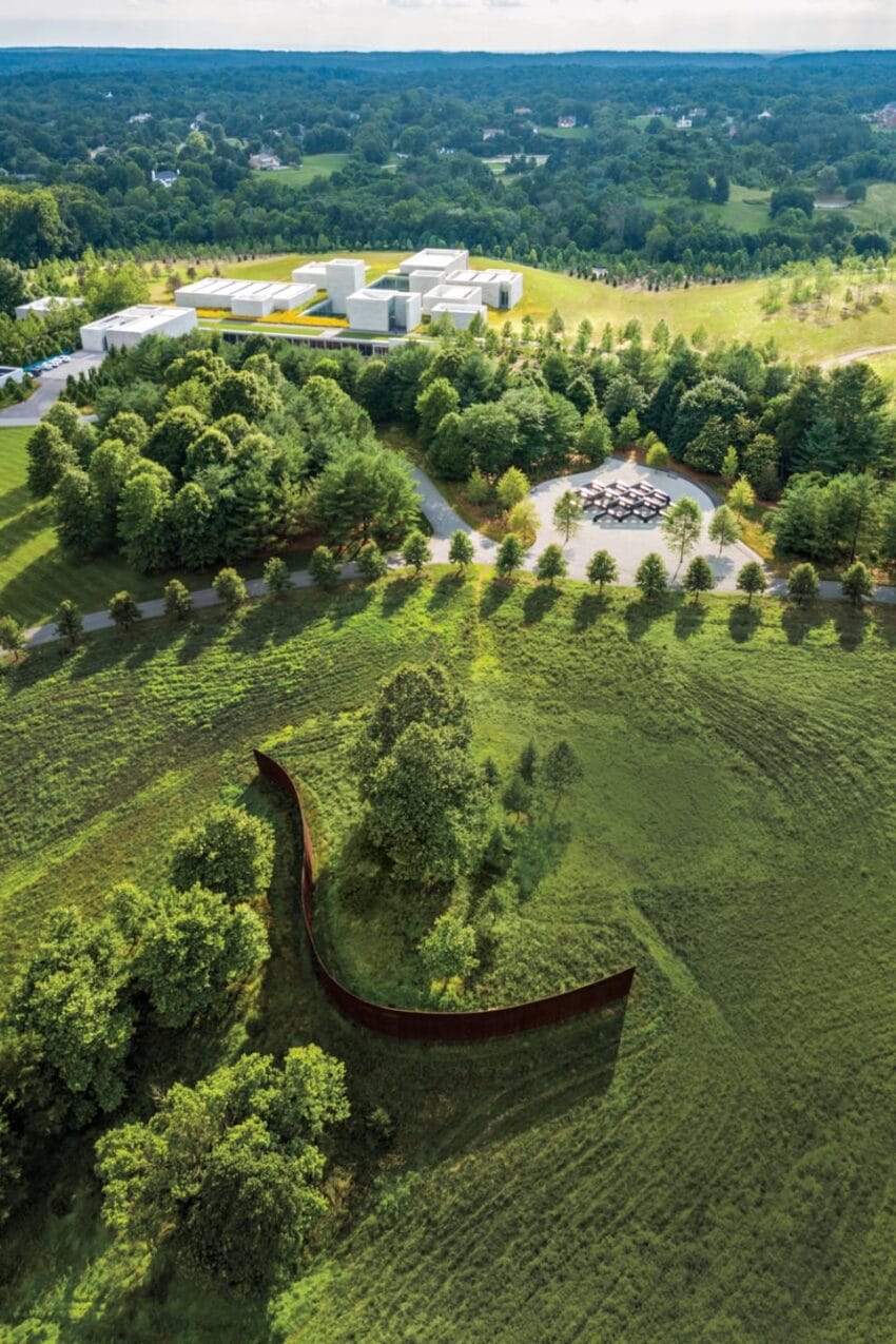 Aerial view of a modern art museum surrounded by lush green landscape and an outdoor sculpture in a field.