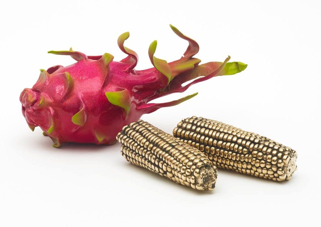 Pink dragon fruit and two metallic golden corn cobs on a white background.