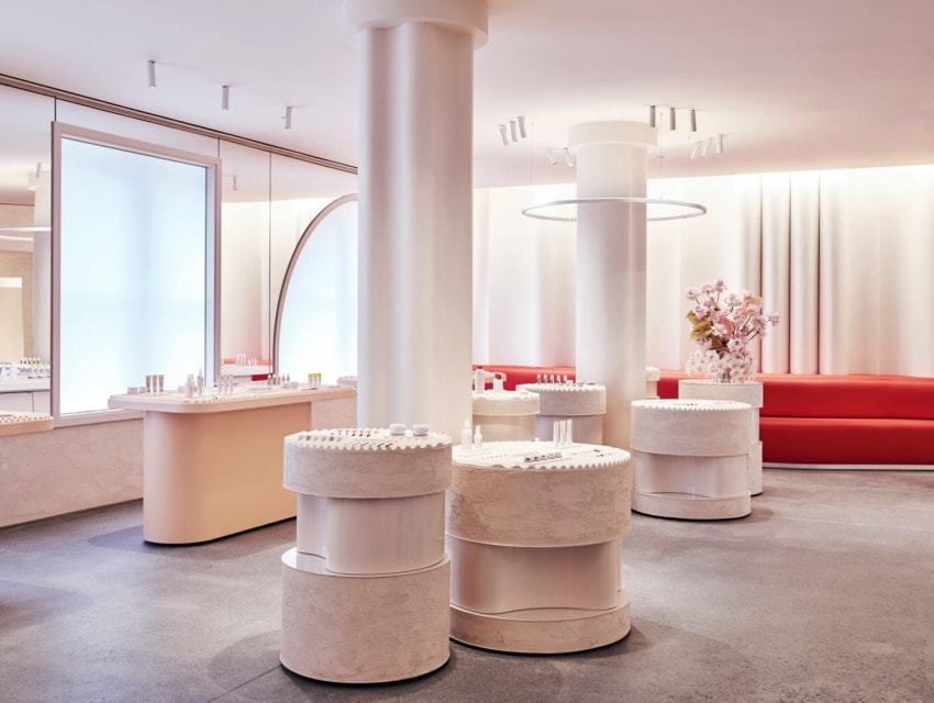 Modern cosmetics store interior with sleek white displays and red seating, featuring elegant lighting and floral decor.