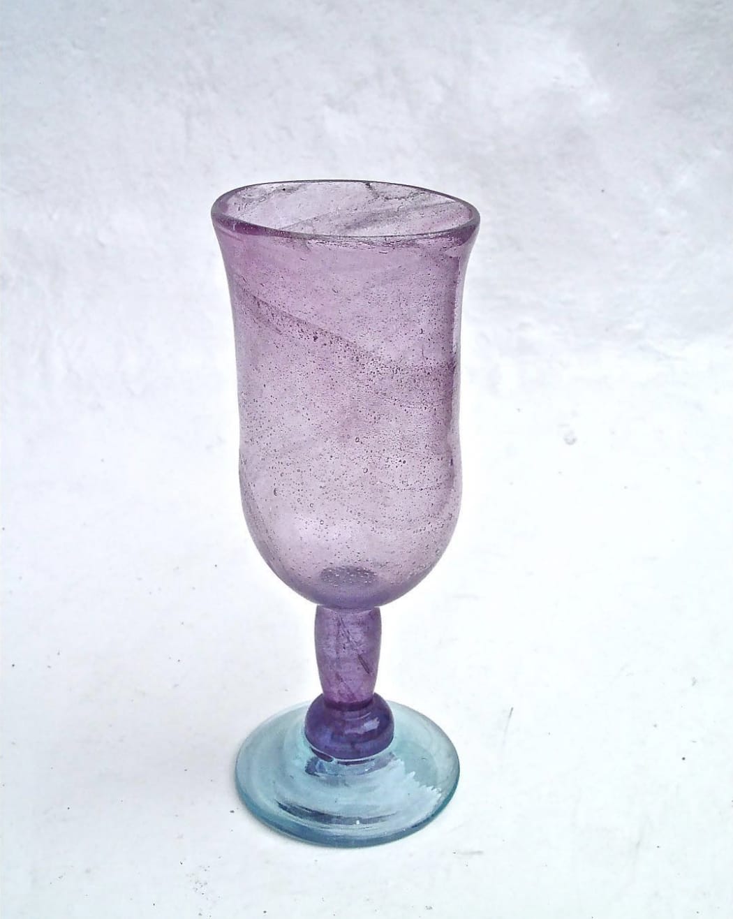 Purple glass goblet with a blue base, set against a white textured background.