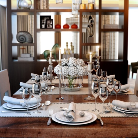 Elegant dining room setup with a wooden table, neatly arranged cutlery, glassware, and a centerpiece of white flowers.