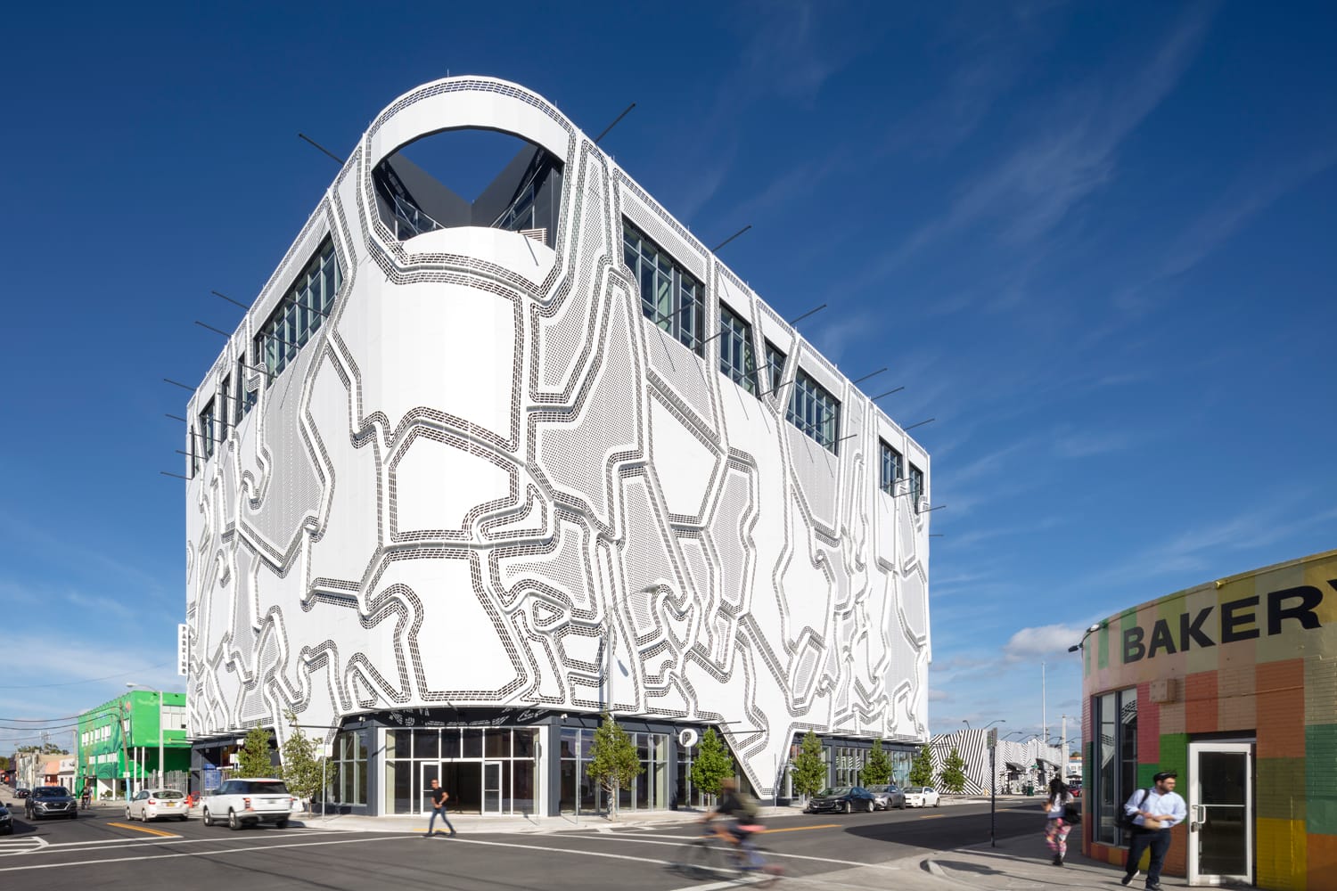 Modern building with a unique geometric facade design under a clear blue sky, located at a busy urban street corner.