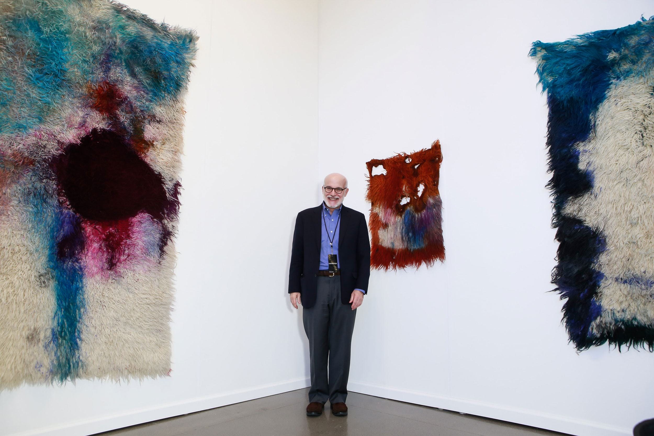 Man standing between two large abstract textile art pieces on a gallery wall.