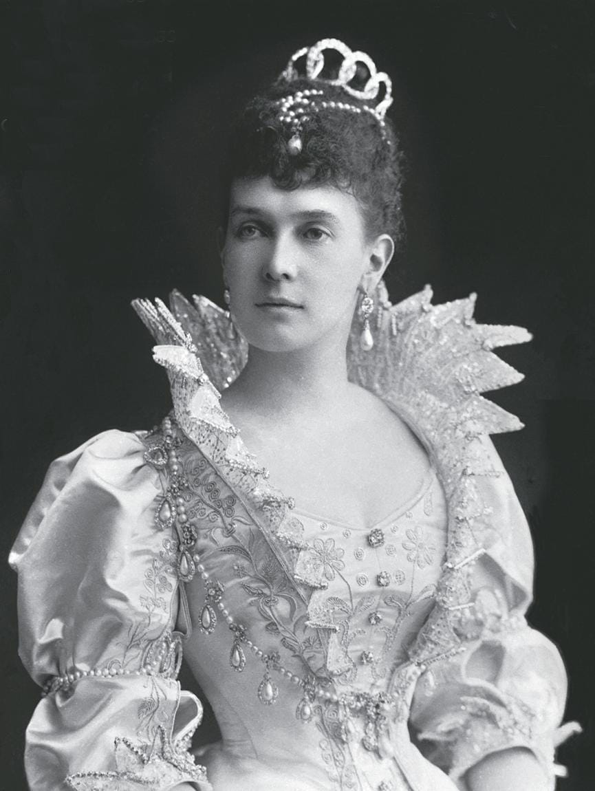 A woman in an ornate Victorian dress with a large collar and a tiara, posing against a dark background.