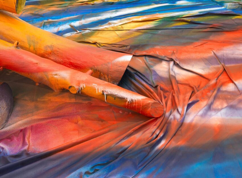 Colorful abstract art with vibrant hues and overlapping textures, featuring painted surfaces and draped fabric.