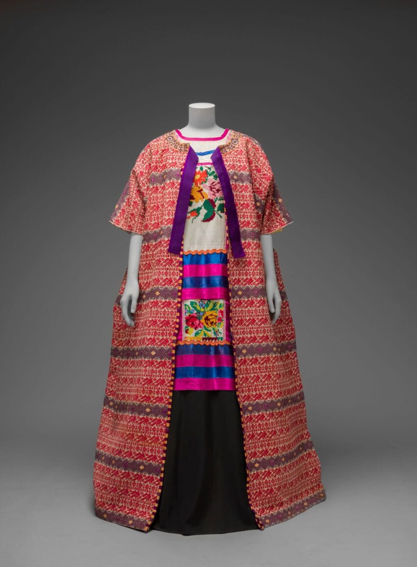 Mannequin wearing a vibrant, traditional embroidered garment with colorful patterns and a flowing design on a gray background.