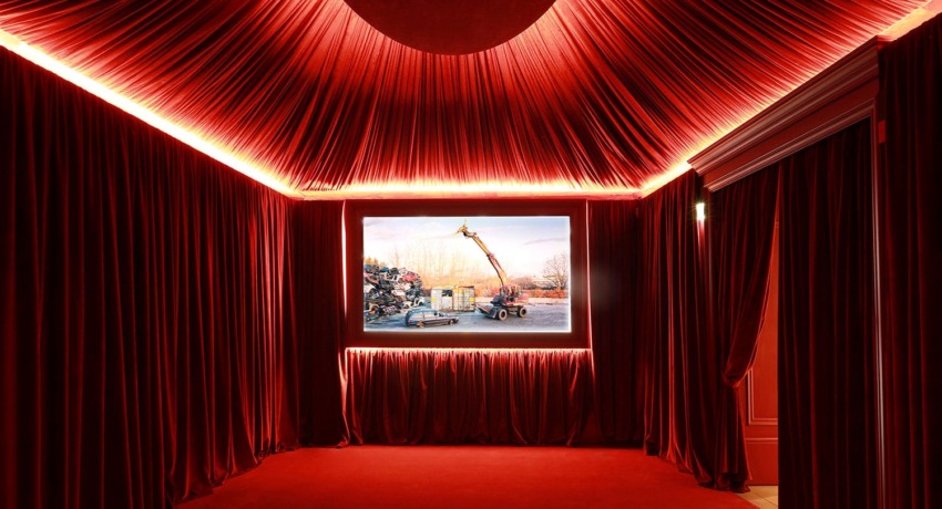 Red velvet-draped room with illuminated photograph of a construction crane in the center, creating a dramatic ambiance