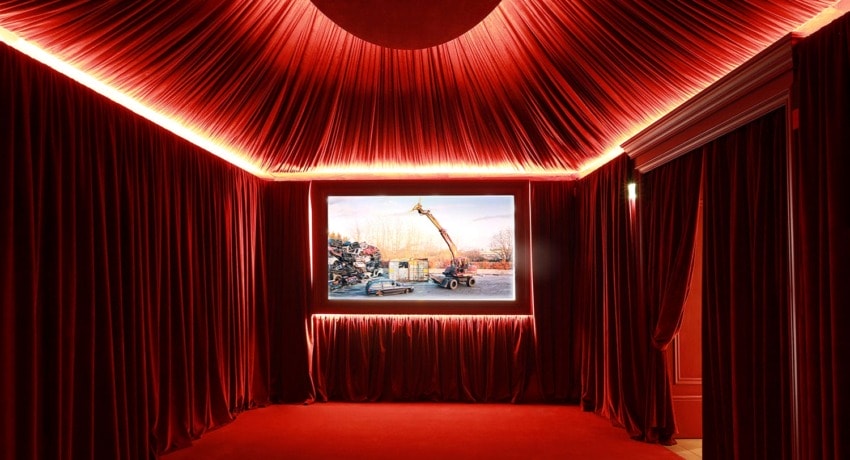 Red velvet-draped room with illuminated photograph of a construction crane in the center, creating a dramatic ambiance
