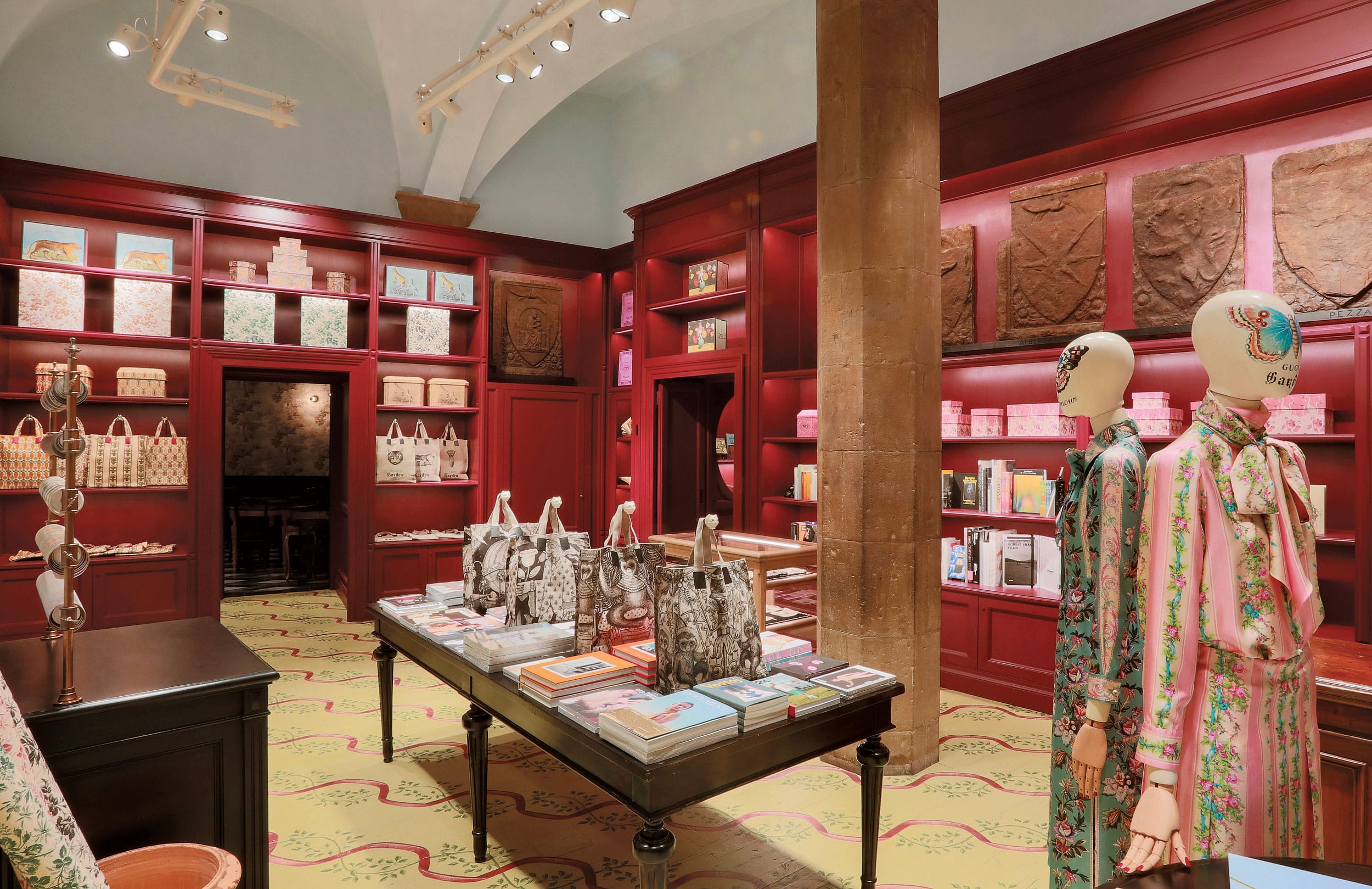 Luxury boutique interior with mannequins, designer handbags, books, and elegantly arranged shelves displaying high-end products.