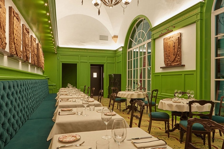 Elegant restaurant interior with green walls, arched window, and tables set for dining with white tablecloths and chairs.