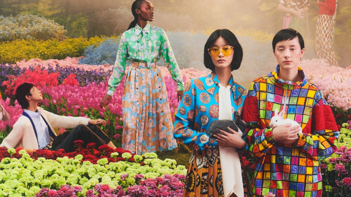 Group of models in vibrant clothing surrounded by colorful flowers, holding rabbits and showcasing diverse fashion styles.