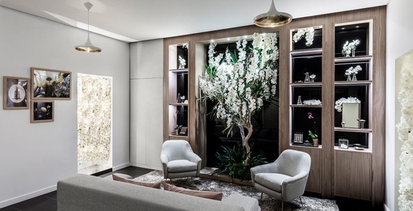Modern lounge with elegant armchairs, a gray sofa, and a backlit wall showcasing artificial white flowers in a cozy setting.