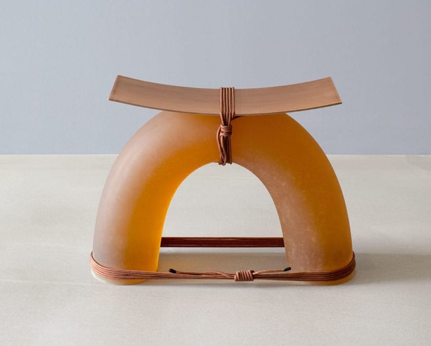Modern sculptural stool with a curved seat and arched base, featuring a rope detail, set against a minimalist background.