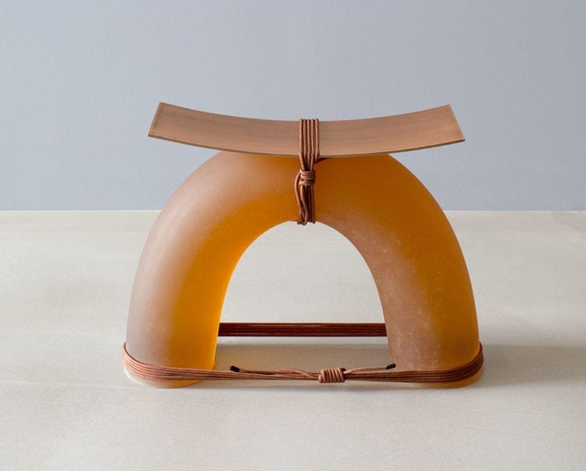 Modern sculptural stool with a curved seat and arched base, featuring a rope detail, set against a minimalist background.