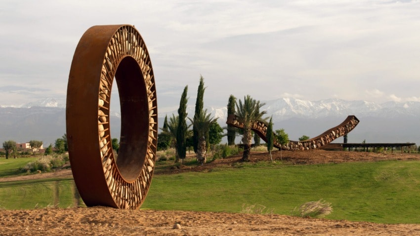 Large circular sculpture in a landscape with trees and distant snowy mountains in the background.