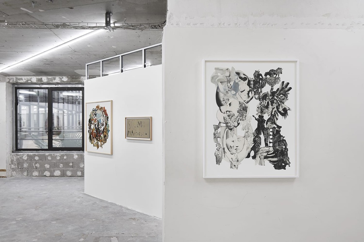 Art gallery interior with framed abstract collage artworks on white walls, concrete floor, and large windows in the background.
