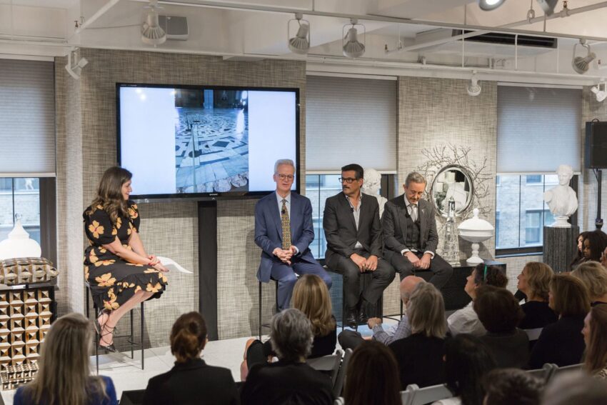 A panel of four people speaking to an audience in a modern, well-lit conference room with artwork displays.