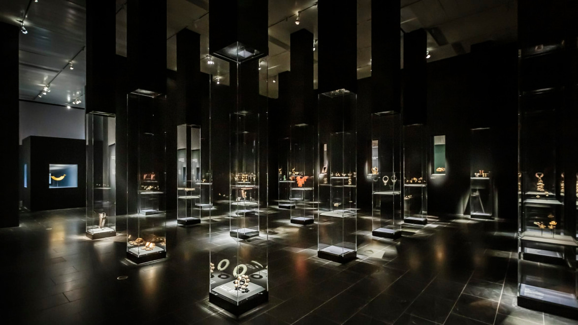 Museum exhibit showcasing ancient golden artifacts displayed in tall glass cases under dim lighting.