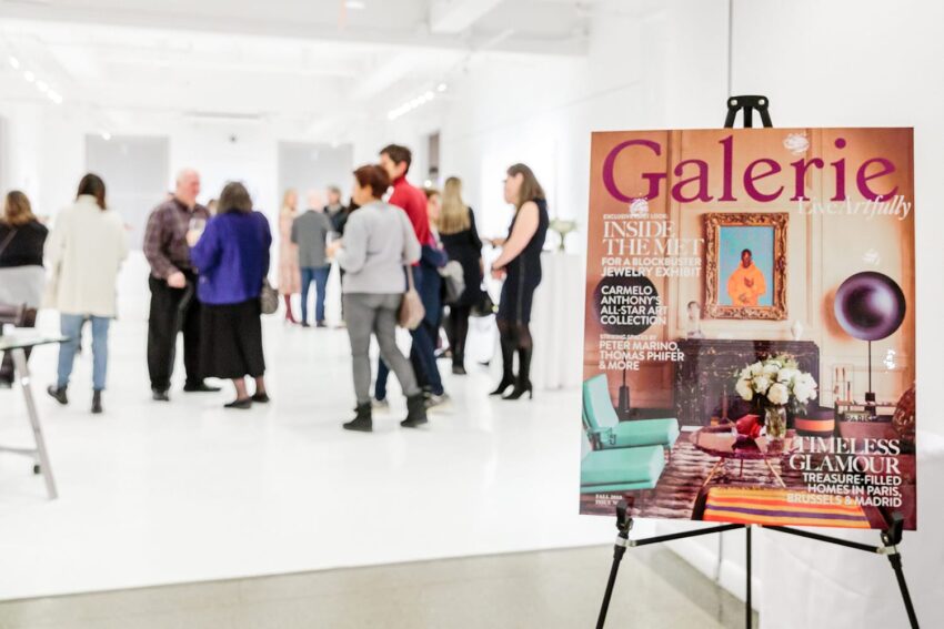 People mingling in an art gallery with a magazine cover on an easel in the foreground.