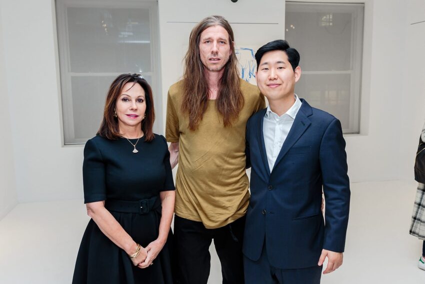 Three people standing in a bright room, one wearing a black dress, another in a yellow shirt, and the third in a suit.