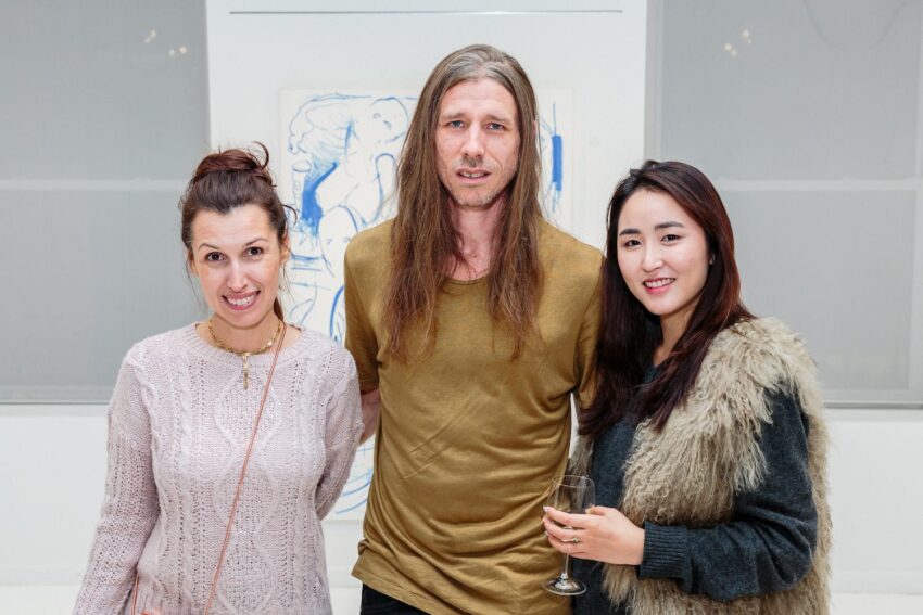 Three people posing at an art gallery, with a painting in the background.