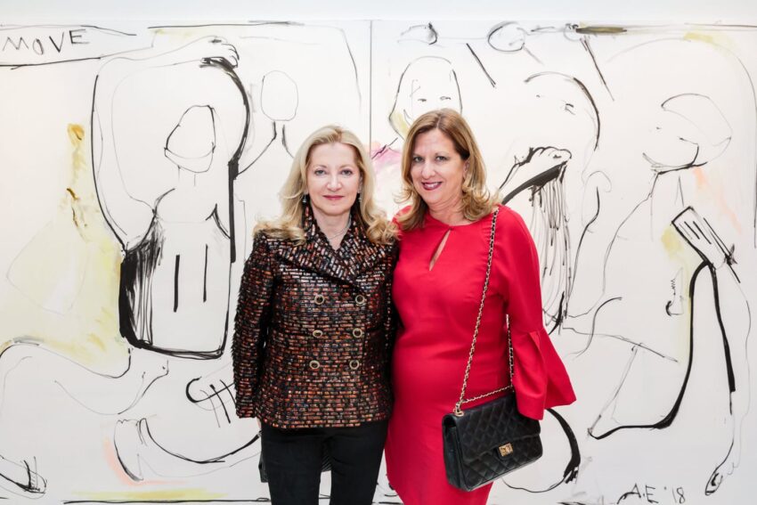 Two women standing in front of an abstract black and white painting with various shapes and lines.