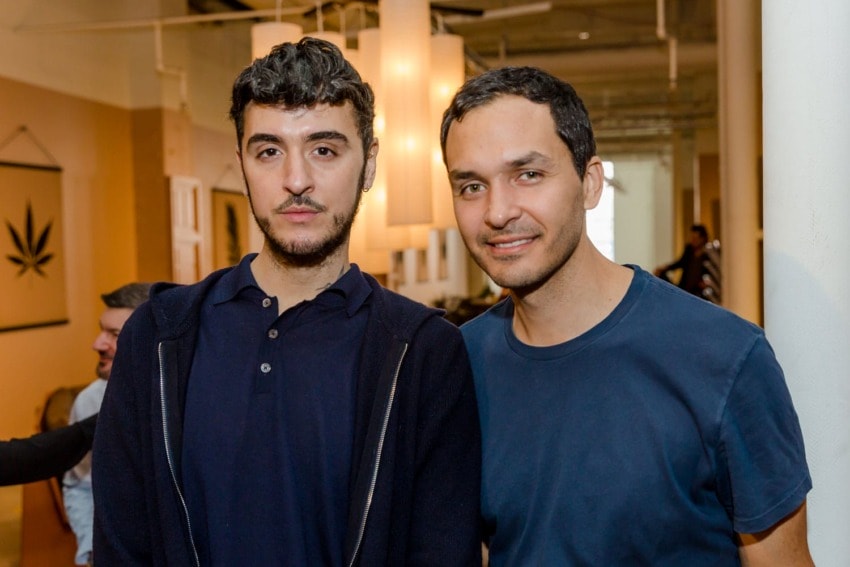 Two people posing and smiling indoors with warm lighting and wall decorations in the background.