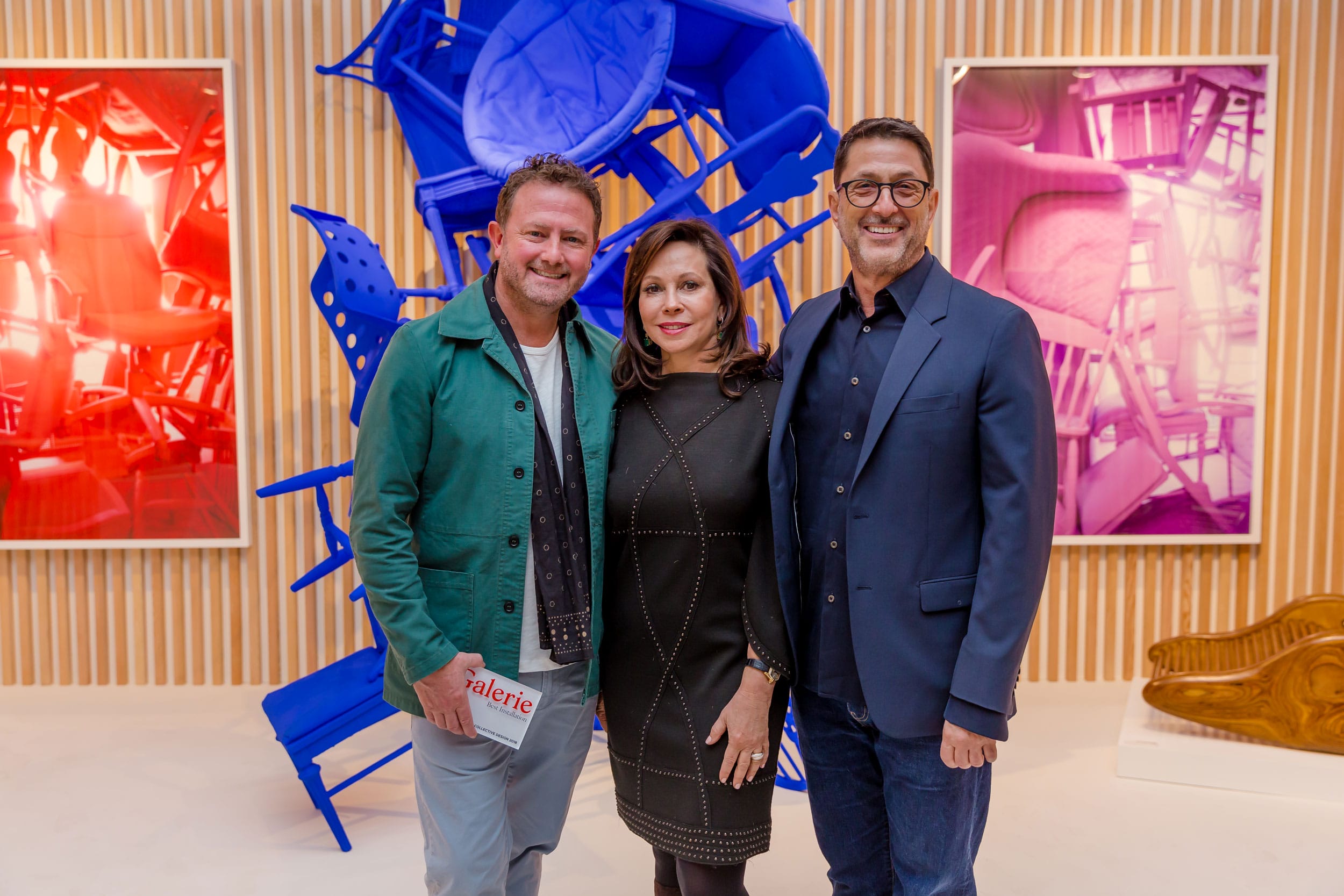 Three people standing together in an art gallery with colorful abstract artwork in the background.