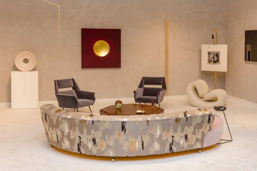 Modern living room with abstract art, patterned sofa, armchairs, and elegant decor elements against a neutral wall.