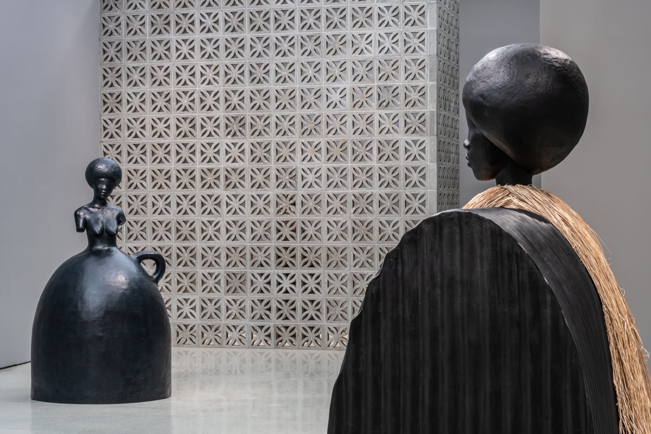 Two abstract sculptures in a modern gallery with a textured wall in the background.