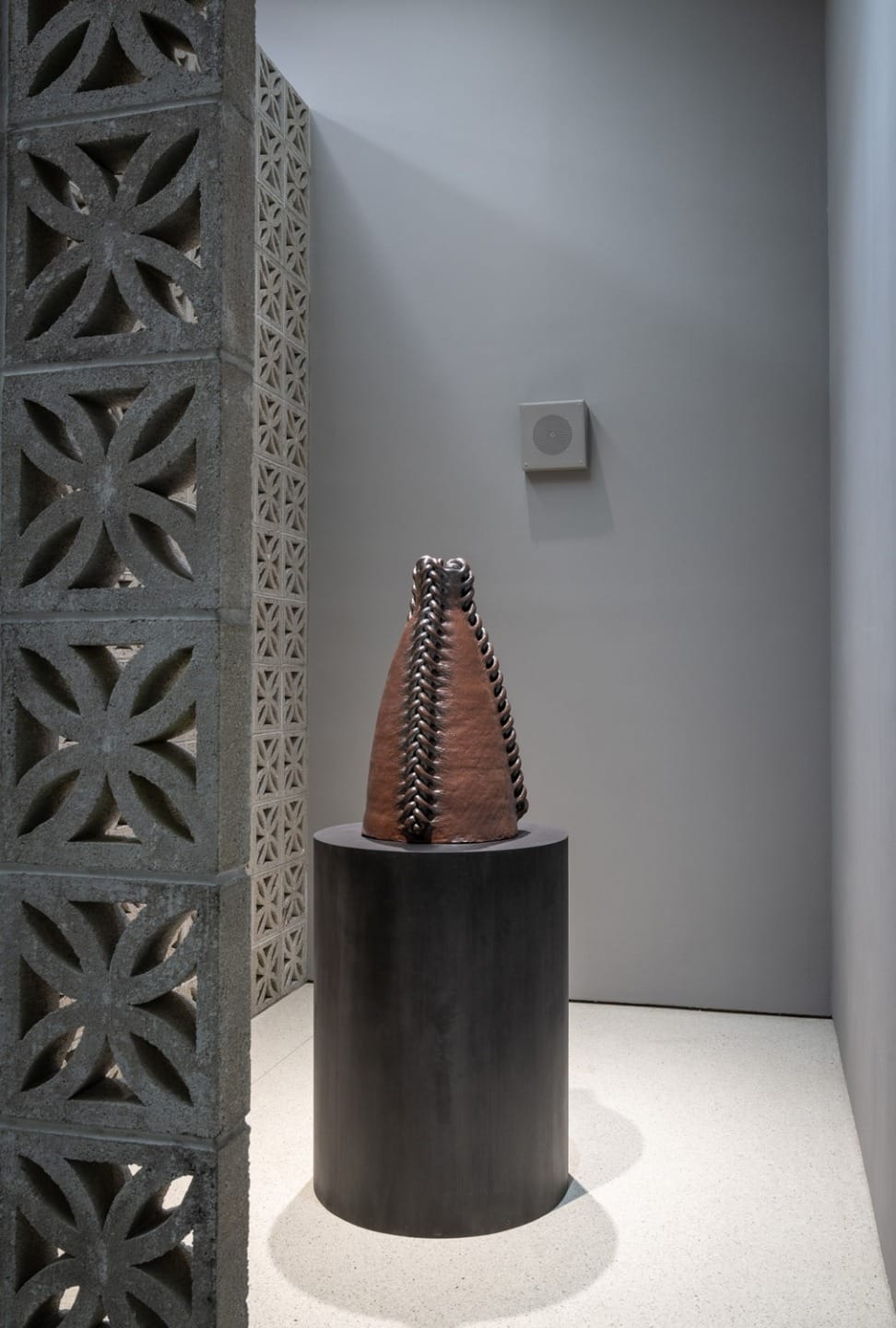 Decorative ceramic sculpture on a black pedestal surrounded by patterned gray walls in a modern minimalist space.