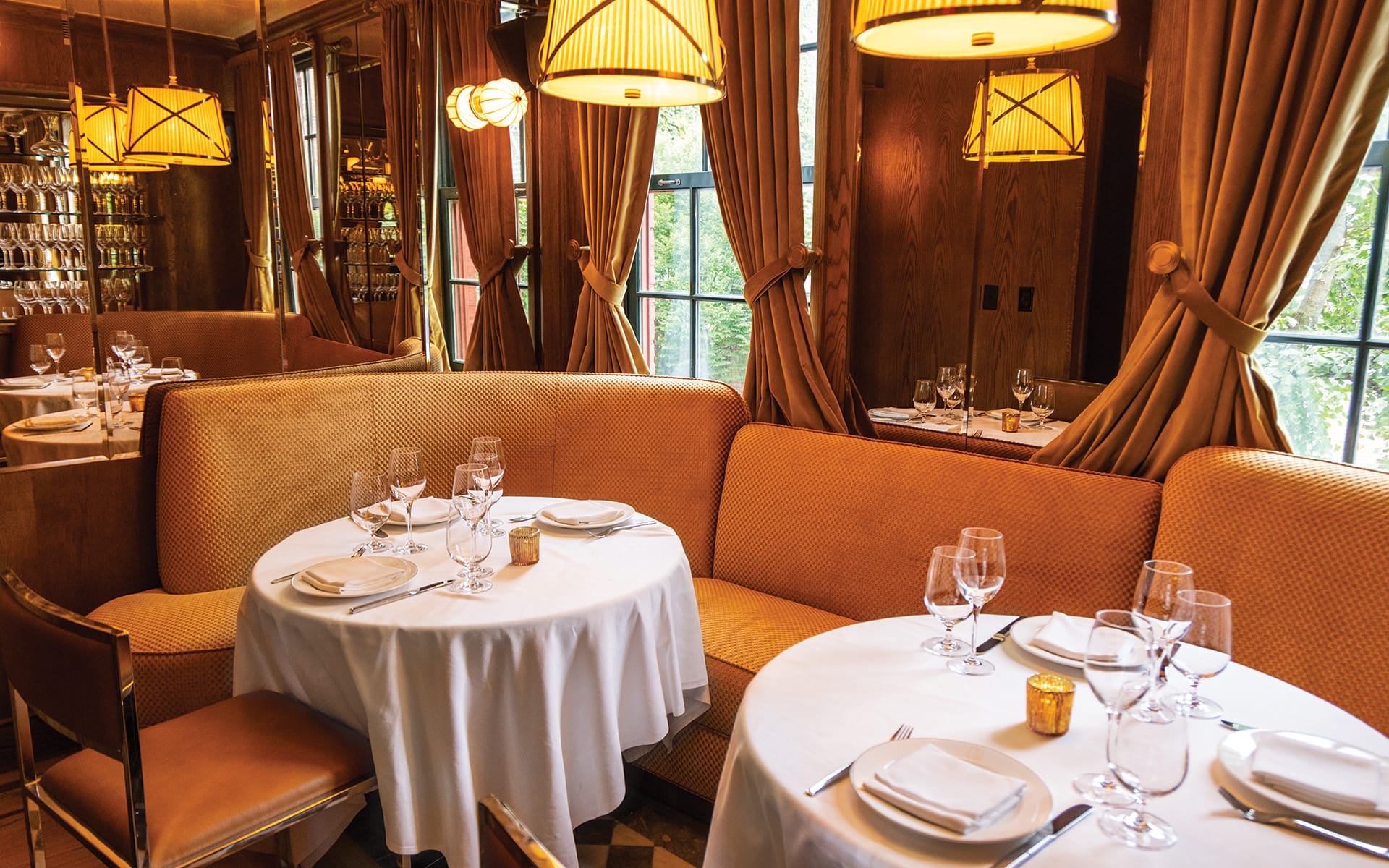 Cozy restaurant interior with elegant table settings, round tables covered in white tablecloths, and warm lighting.