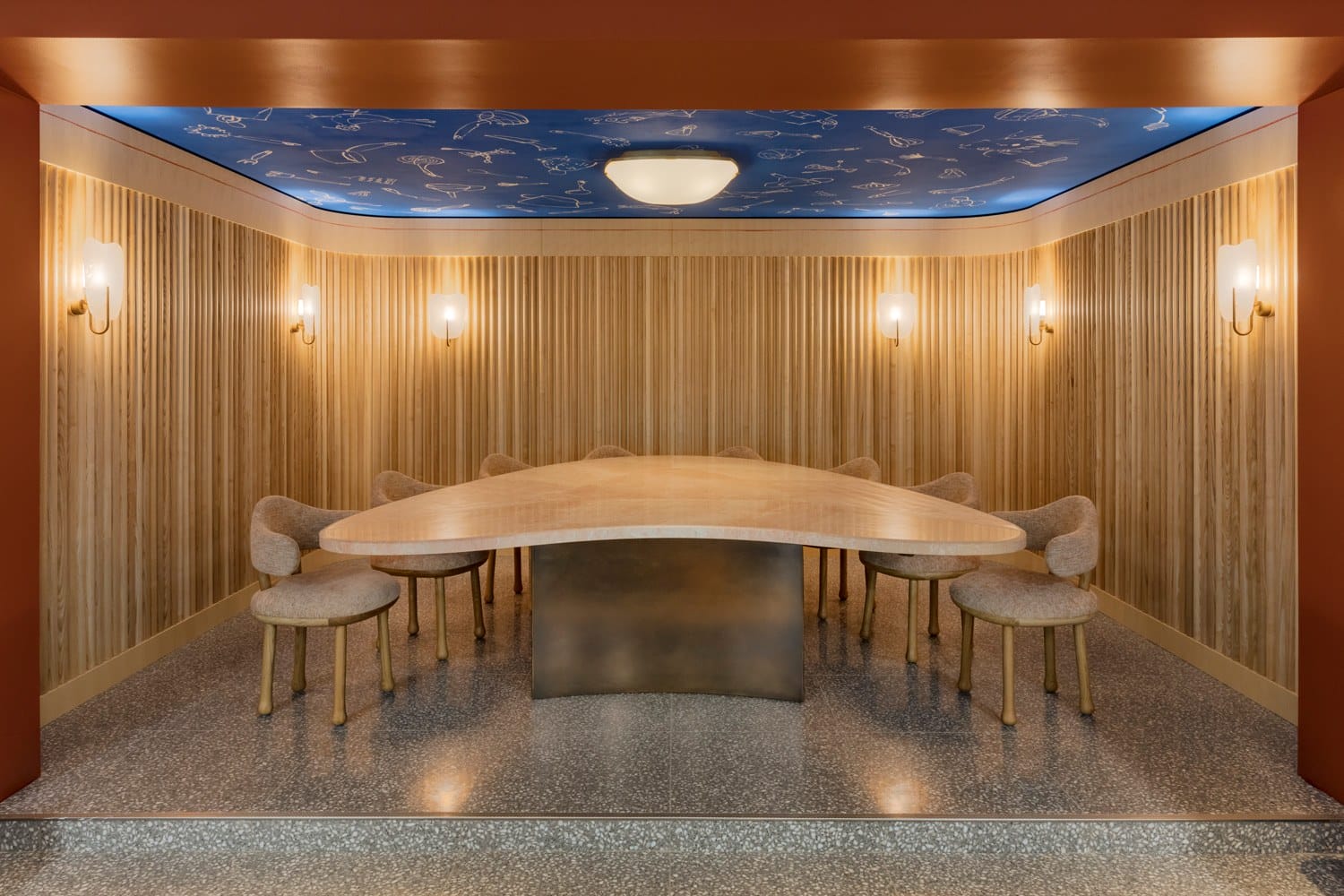 Modern dining area with a unique triangular table, upholstered chairs, wood paneling, and constellation-themed ceiling.