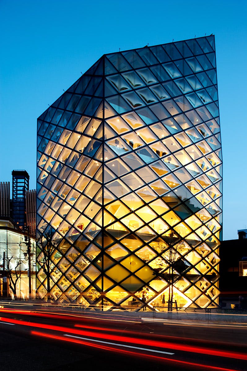 Modern glass building illuminated at night with a unique geometric design, featuring a crisscross pattern on the facade.
