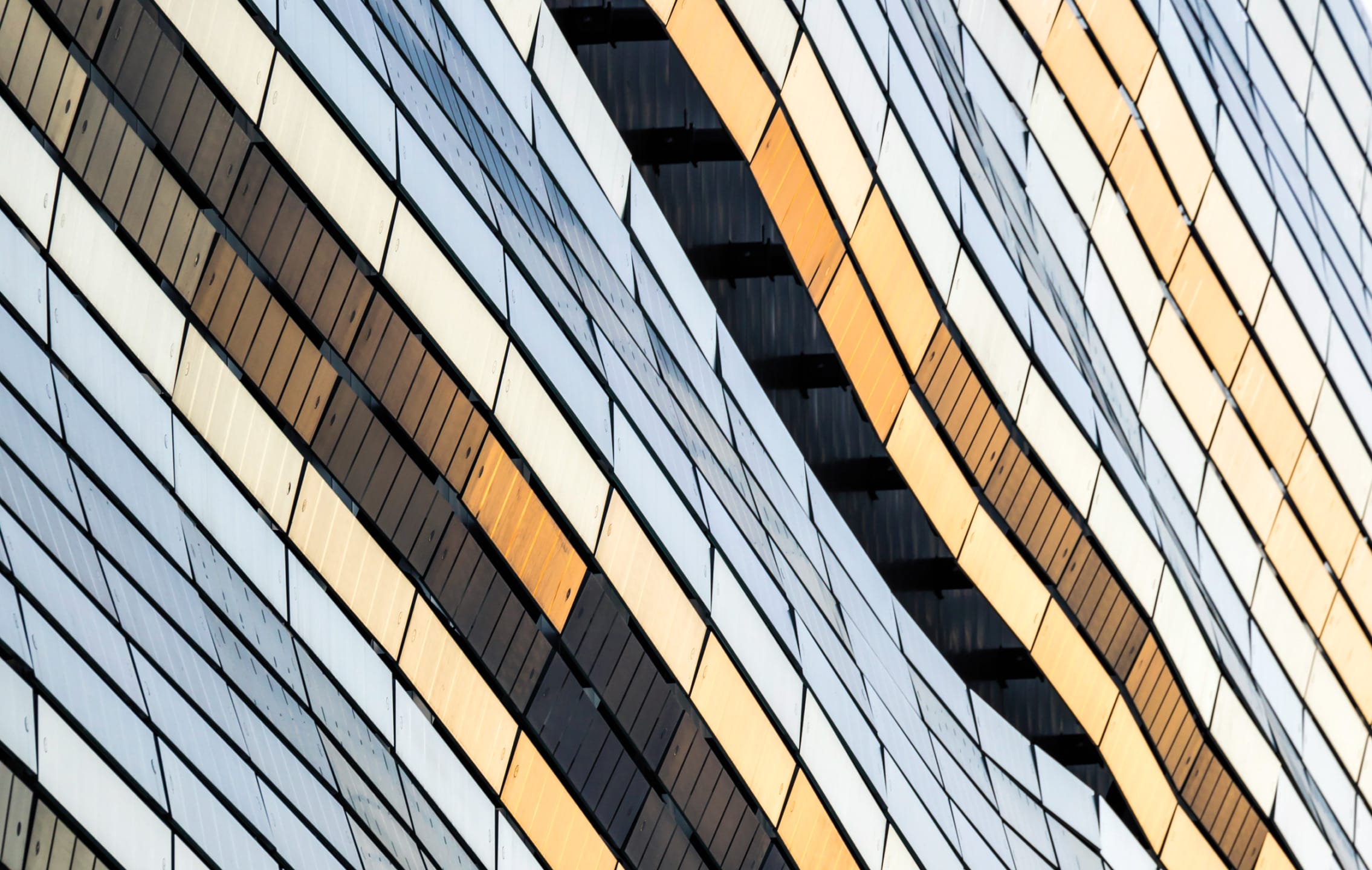 Close-up of modern building facade with wavy, alternating black and gold reflective panels creating a dynamic pattern.