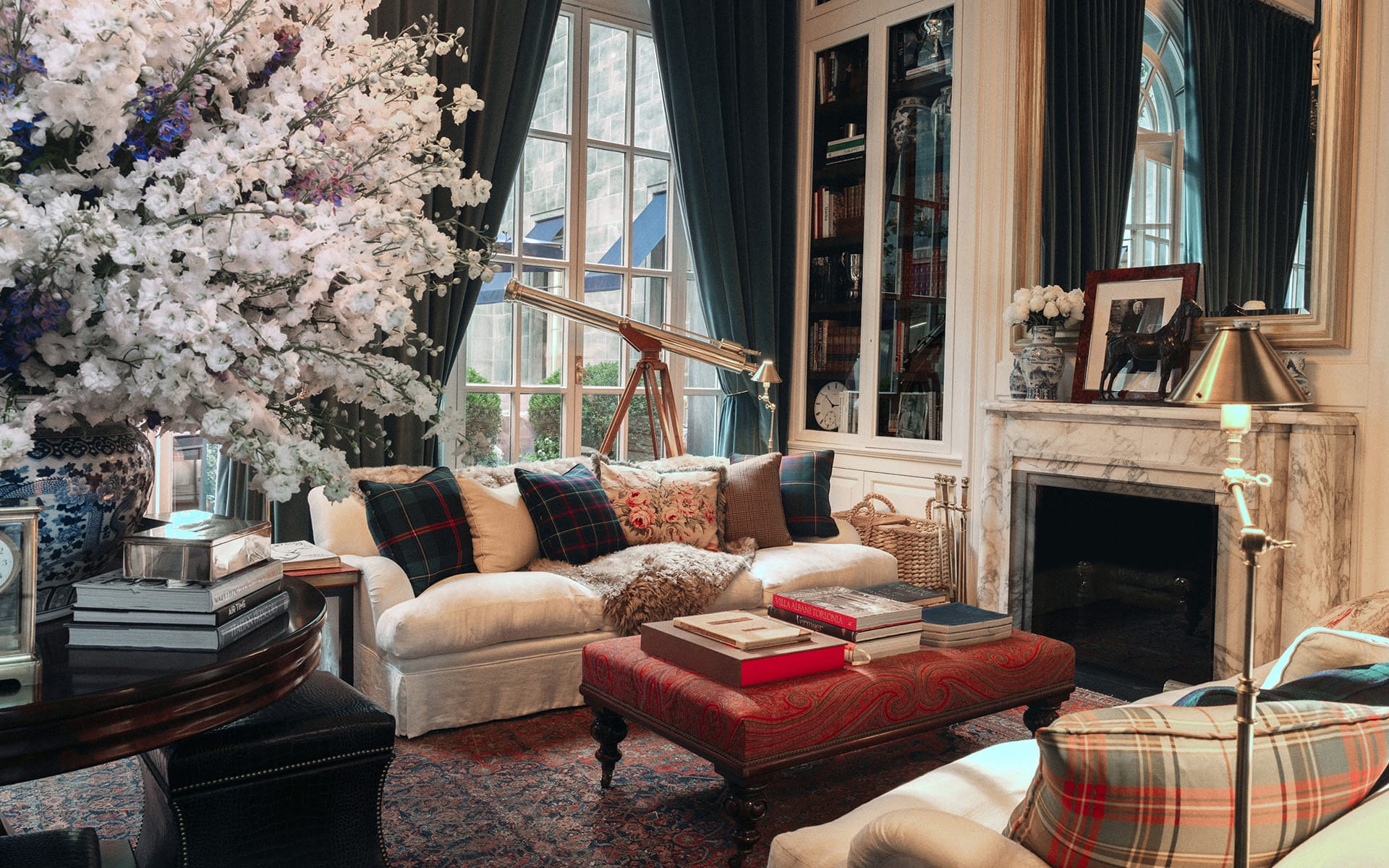 Elegant living room with classic decor, cozy sofa, floral arrangement, telescope by the window, and books on a red ottoman.