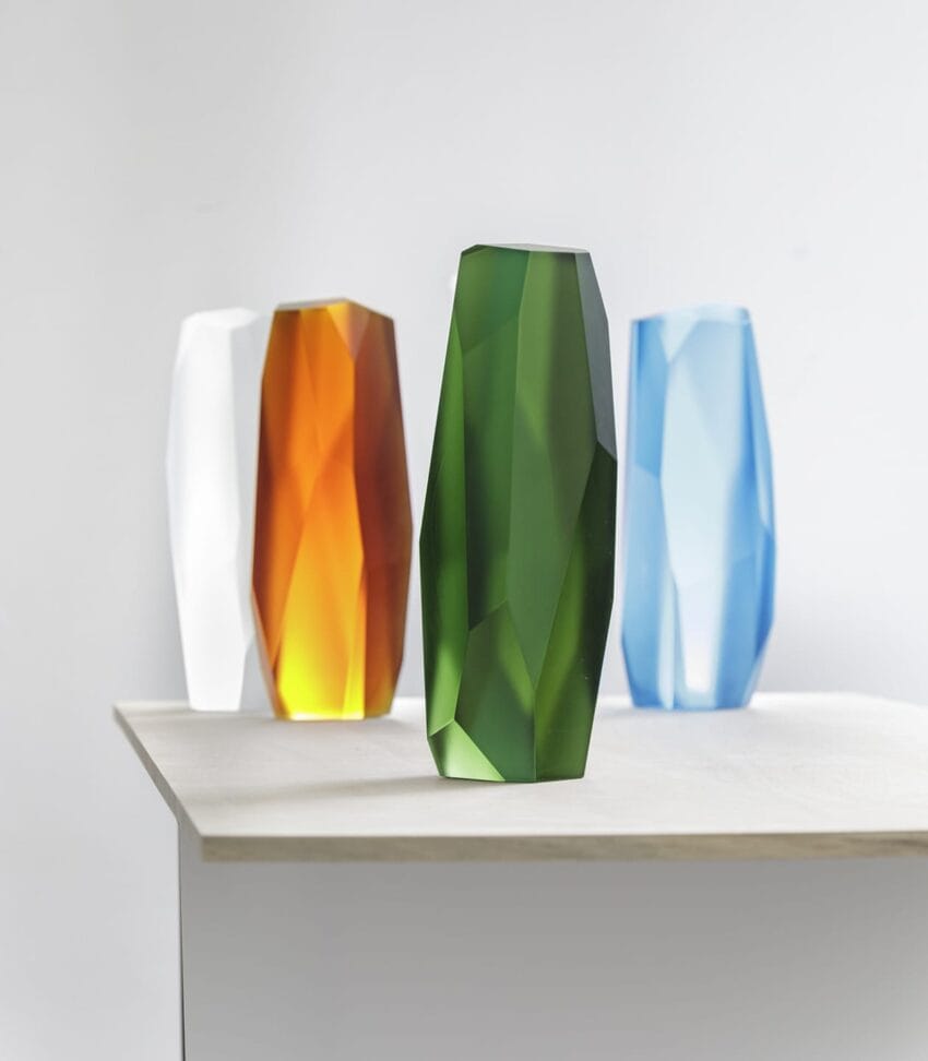 Colorful geometric vases on a table with a green vase in the foreground and white, orange, blue vases in the background