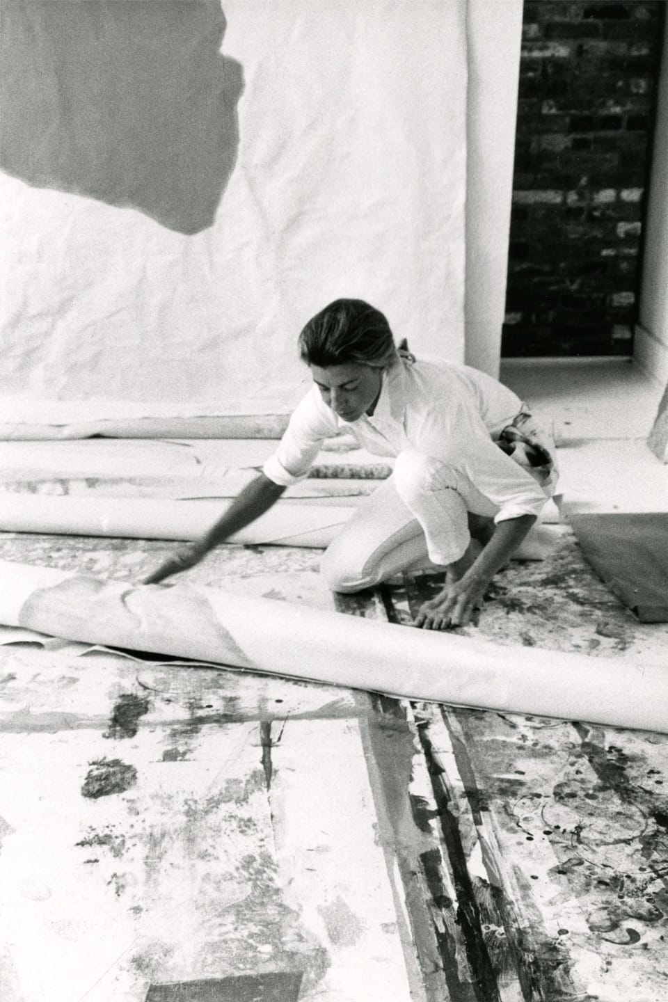 Artist kneeling on floor, working on large canvas with abstract patterns in a studio setting.