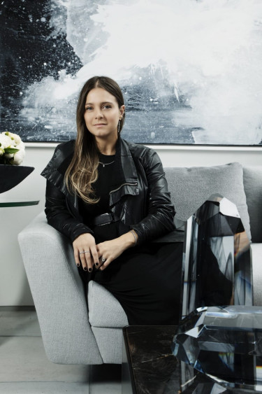 Person sitting on a couch with black leather jacket, next to a modern art piece and decorative crystals in a contemporary setting.