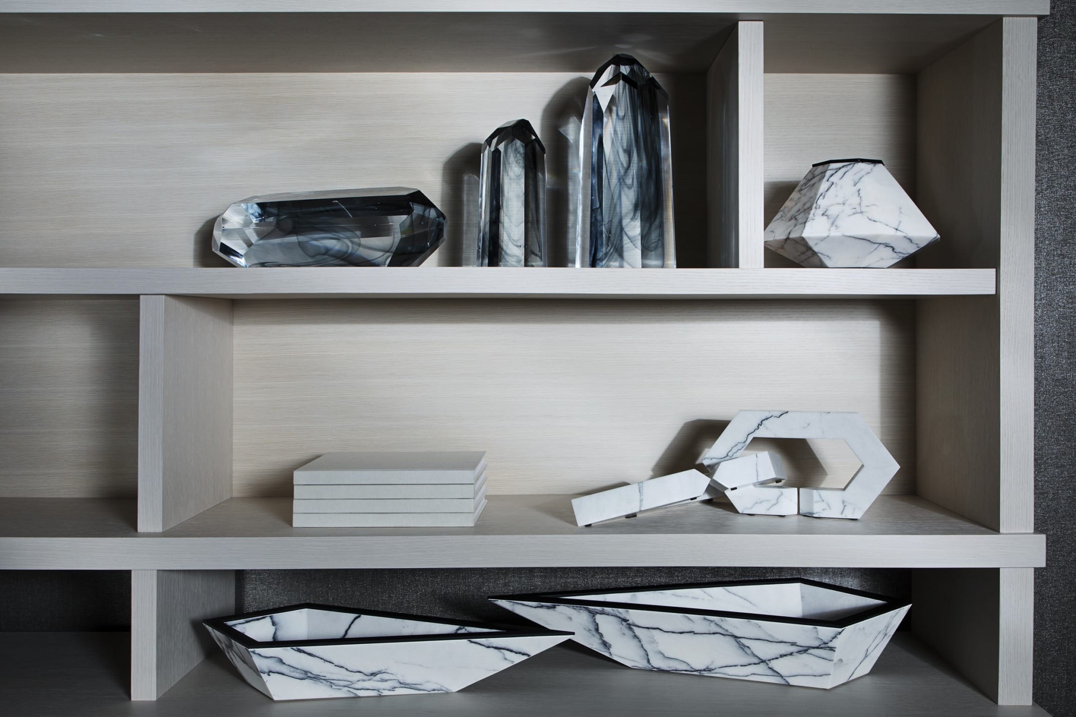 Shelf displaying geometric marble sculptures and books, featuring a modern and artistic design aesthetic.