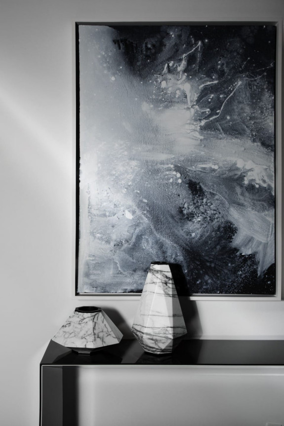 Abstract black and white painting on wall behind two marble-patterned vases on a sleek black table.