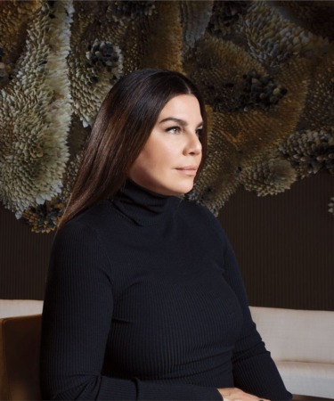 Person sitting in profile with a dark floral background wearing a black turtleneck sweater.