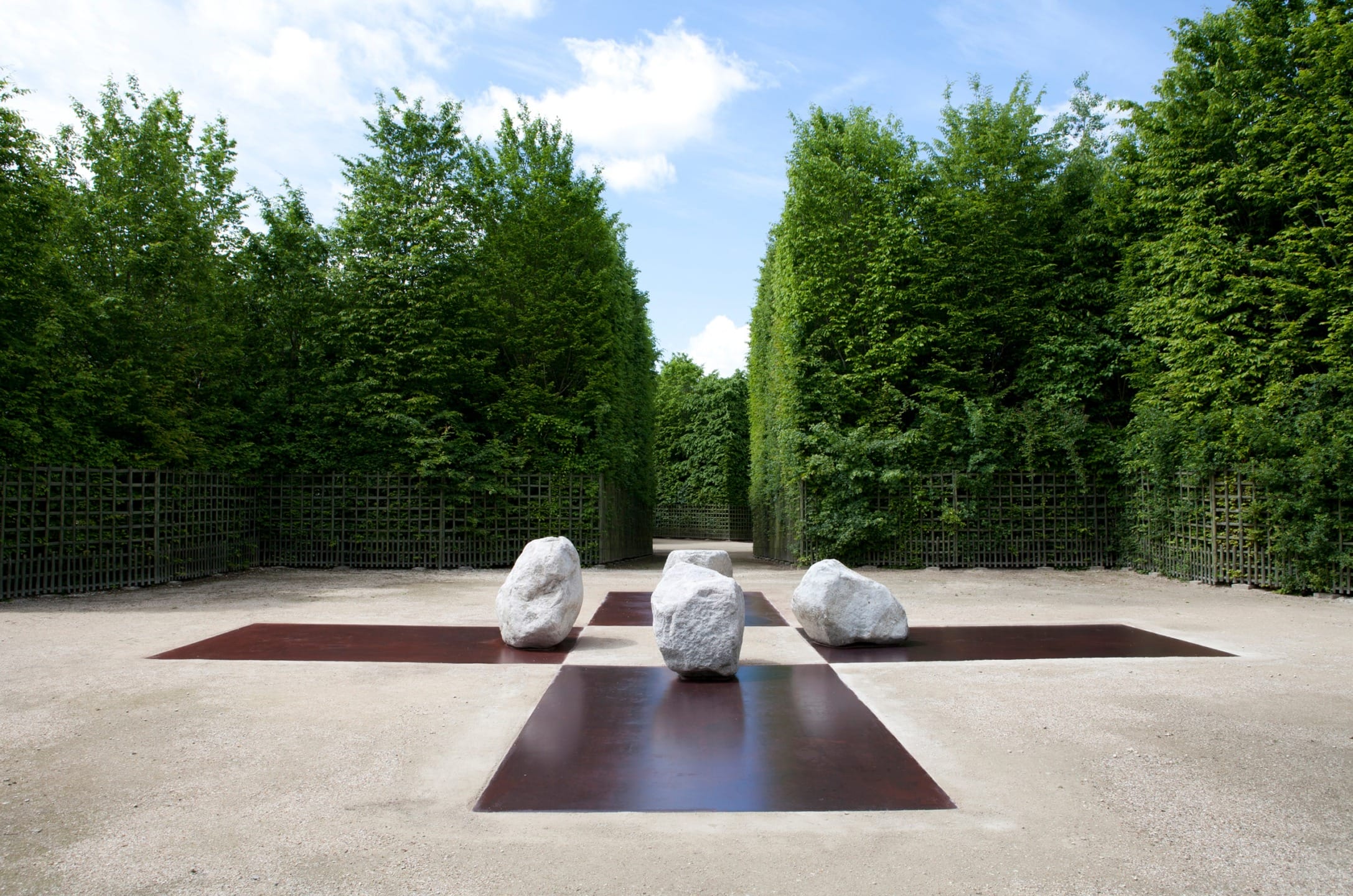 Three large white stones on a modern landscape design with greenery and a clear blue sky in the background.