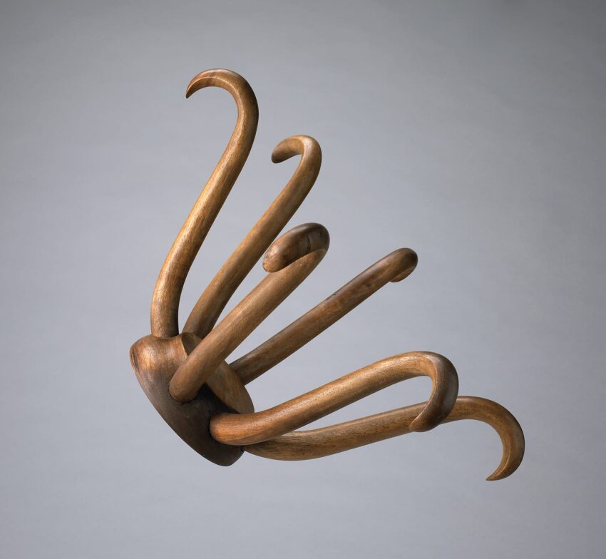 Abstract wooden sculpture with multiple curved, elongated arms extending from a central base on a gray background.
