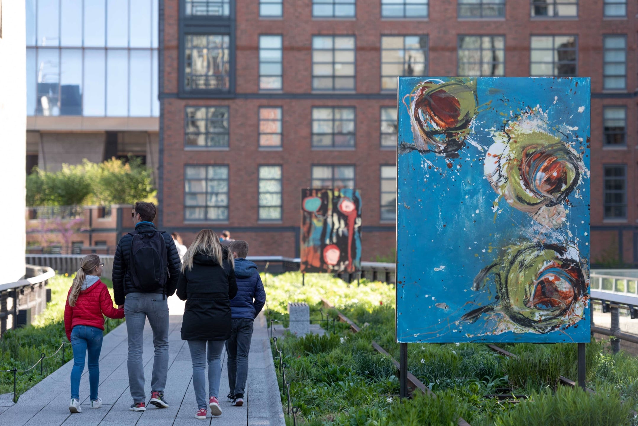 Family walking along a path with artwork and buildings in the background