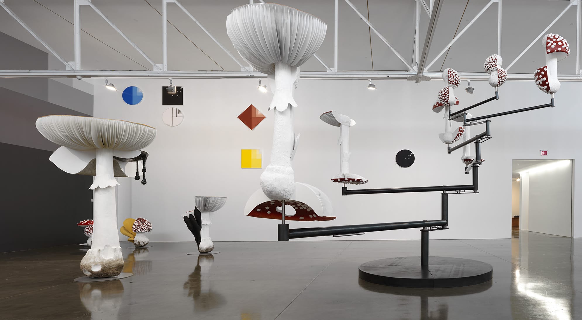 Modern art installation featuring large mushroom sculptures and abstract geometric shapes on display in an open gallery space.