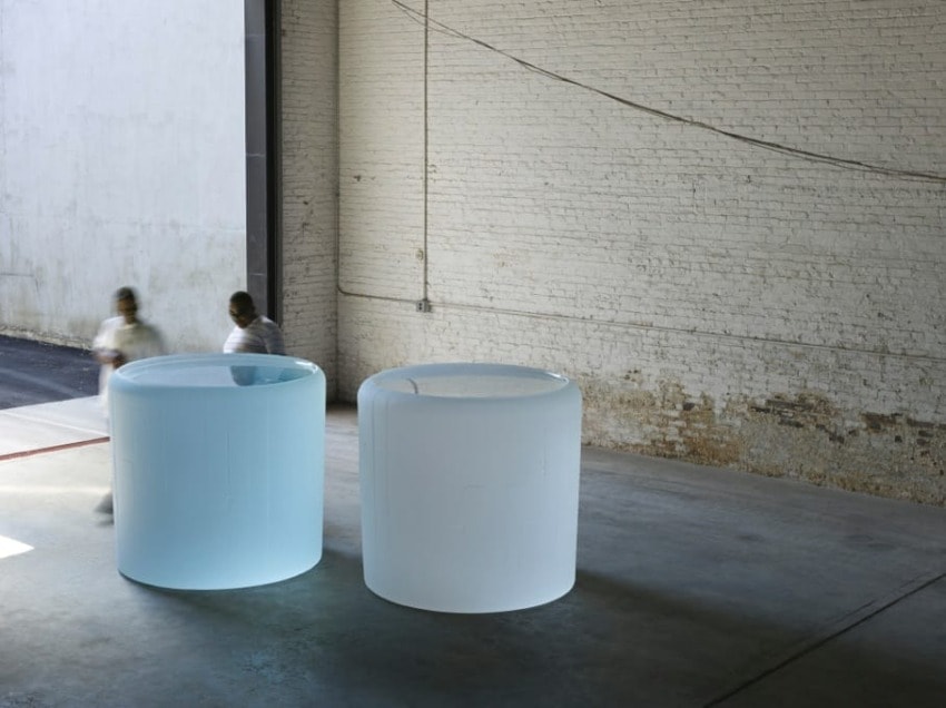 Two large cylindrical sculptures, one blue and one white, in a spacious industrial room with two people walking by.