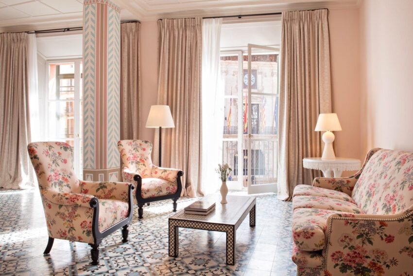 Elegant living room with floral armchairs, sofa, patterned floor, two lamps, and balcony view through large windows.